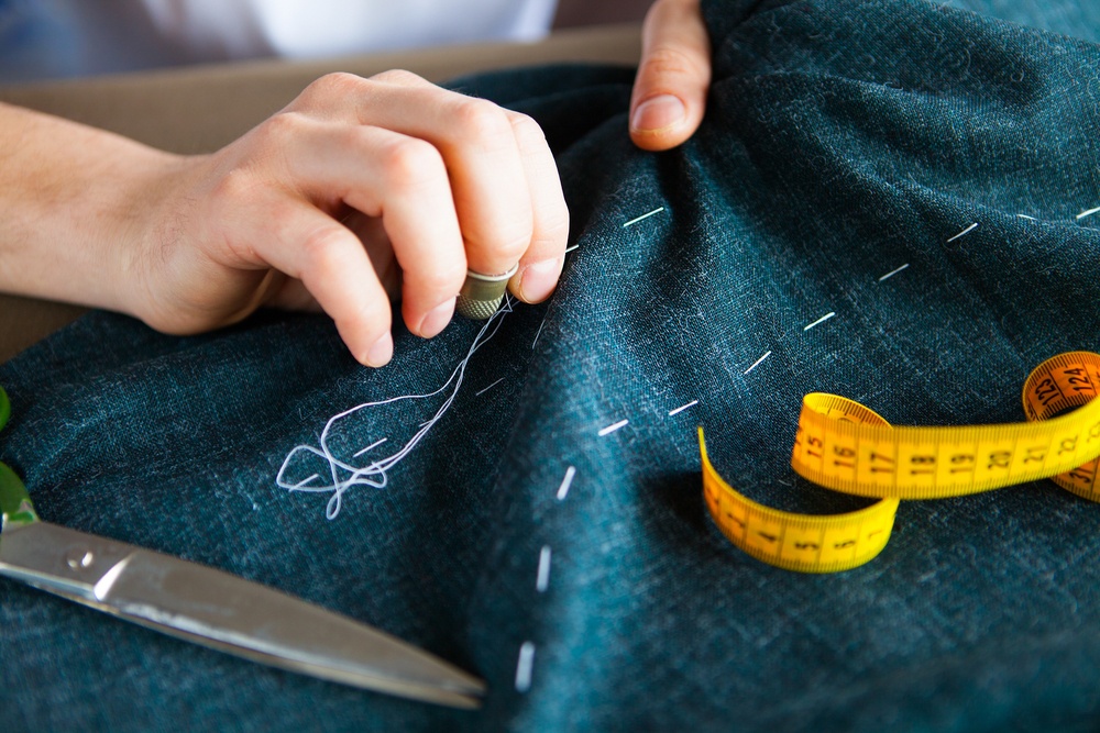 man working in his tailor shop doing hand stitching a cloth with needle